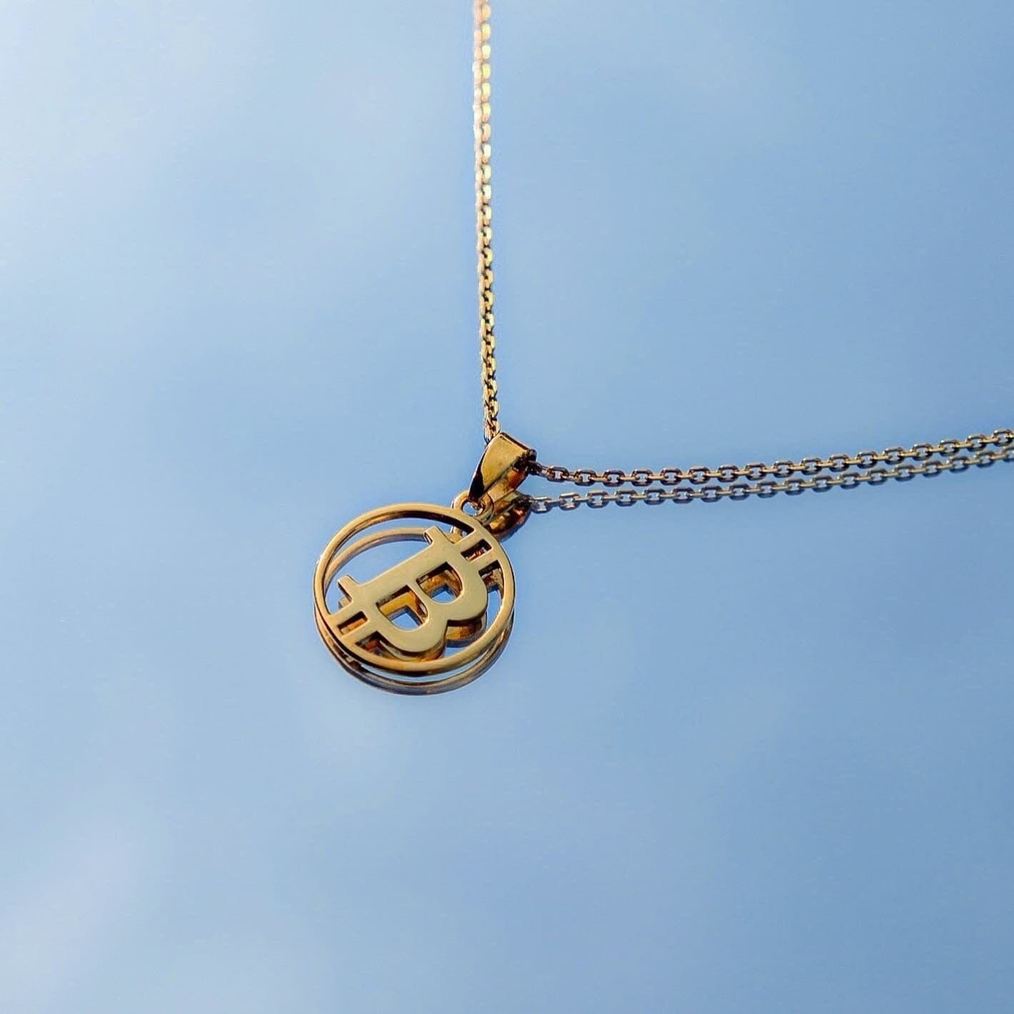BTC Pendant in gold plating held against an open sky